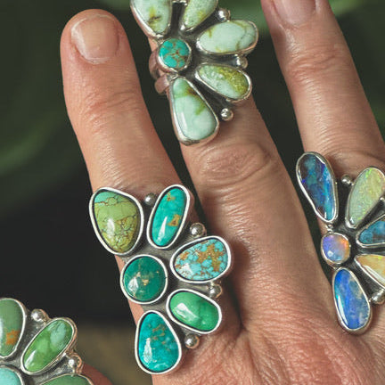 Hand wearing multiple floral-patterned rings with gemstones on a blurred natural background