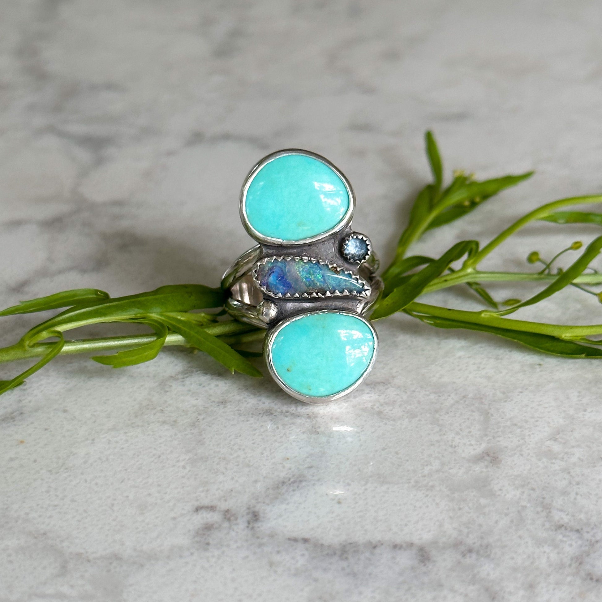 Close up of Handcrafted silver ring featuring an oval turquoise stone, set in an intricate bohemian-inspired band, showcasing natural patterns.