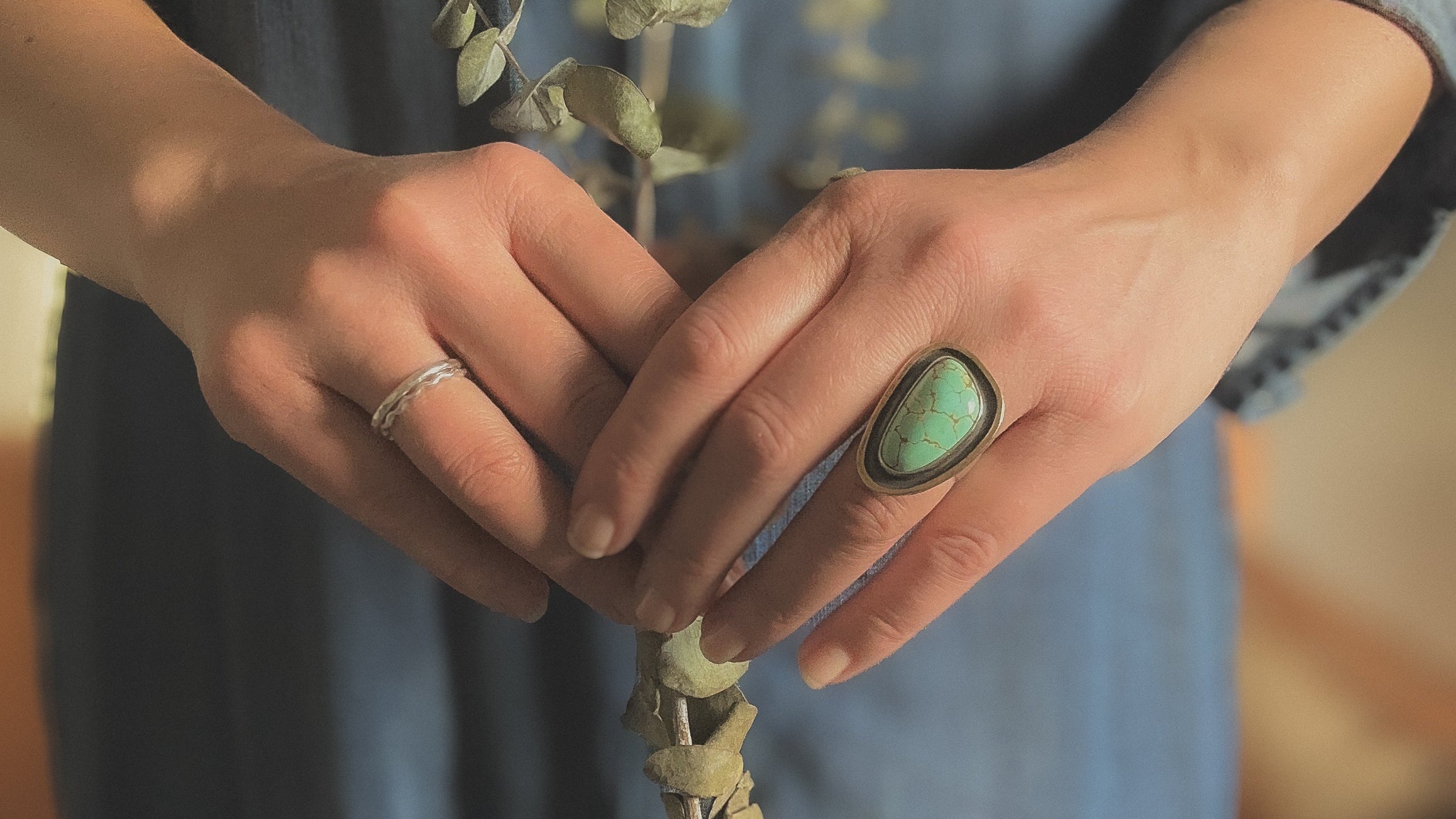Close-up of hands holding a plant with one hand wearing a ring featuring a turquoise stone.
